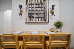 Een eetruimte met een houten tafel gedekt voor vier personen, twee wandlampen en een potplant op tafel.