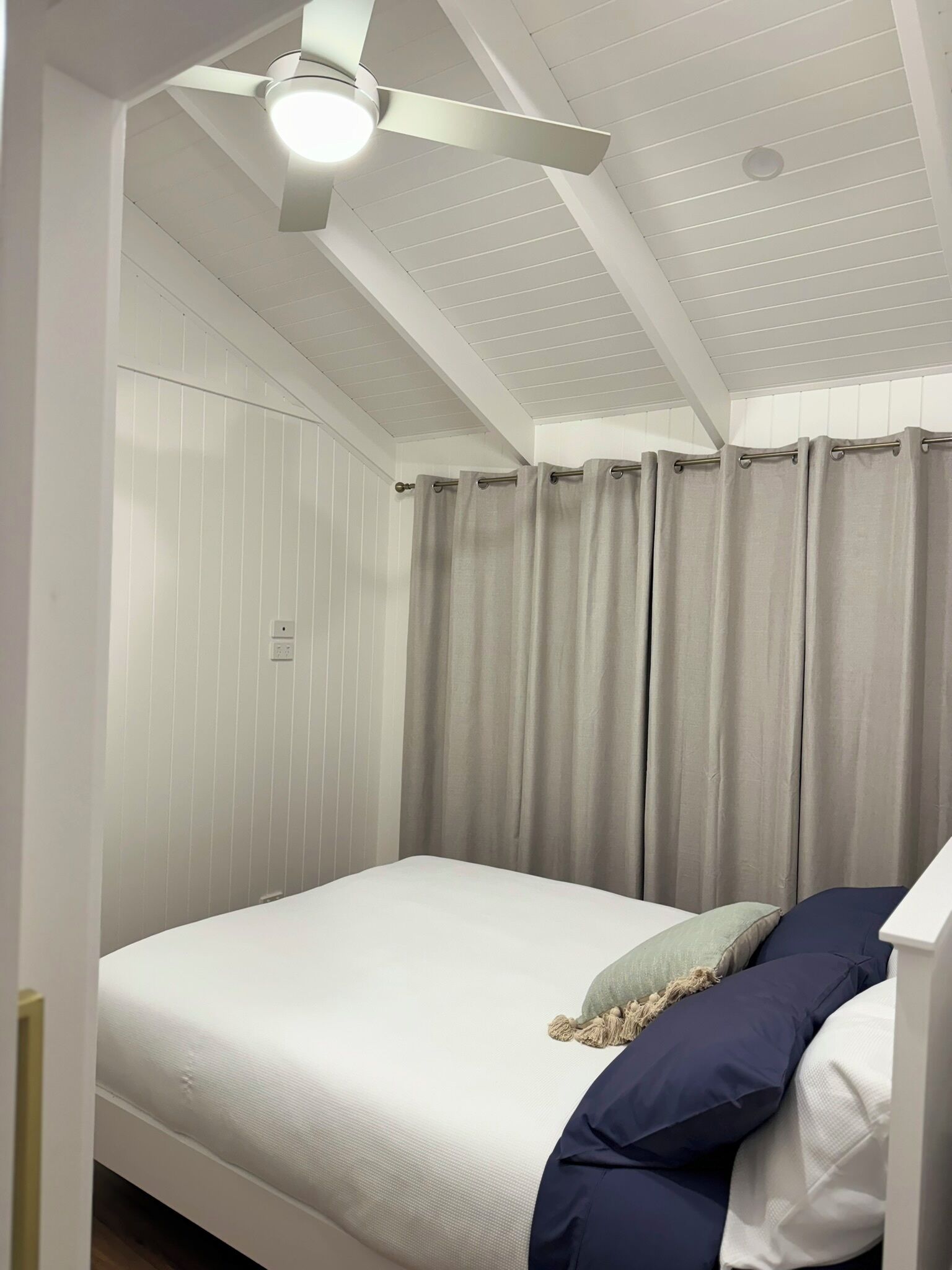A bedroom with a bed, a ceiling fan, and a window with curtains.