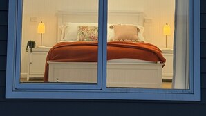 A bedroom with a large window, white walls, and a bed with a red blanket. - Kingdom Cottages (Gulgong)