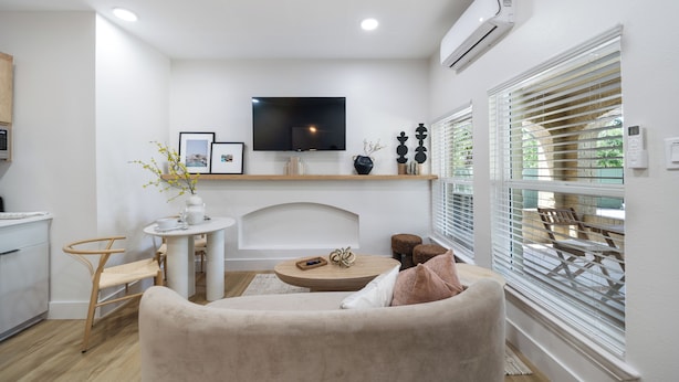 A modern living room with a flat-screen TV, a fireplace, a dining area, and a large window with blinds. - Mediterranean Villa Vibes #1 at East Downtown (Houston)