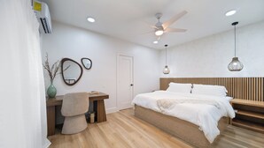 A modern bedroom with a wooden bed, a desk, a chair, a mirror, and a ceiling fan. - Mediterranean Villa Vibes #1 at East Downtown (Houston)