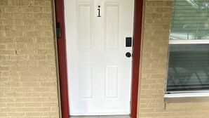 A white door with a red frame, a small mailbox, and a window with blinds. - Mediterranean Villa Vibes #1 at East Downtown (Houston)