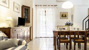 A living room with a sofa, a TV, a dining table with chairs, and a window with curtains.