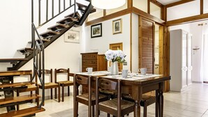 A dining area with a wooden table, chairs, a vase of flowers, and a staircase.