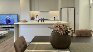Une cuisine moderne dotée d’un îlot central, d’un coin repas avec une table et des chaises, et d’un téléviseur diffusant un programme d’information.