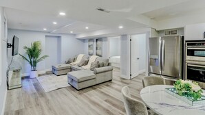 A modern living room with a grey sectional sofa, a dining table with a glass centerpiece, and a kitchen area with stainless steel appliances. - Luxurious Unit in Hyde Park (London)