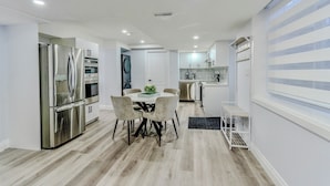 A modern kitchen with a built-in oven, a stainless steel refrigerator, and a dining area with a round table and chairs. - Luxurious Unit in Hyde Park (London)