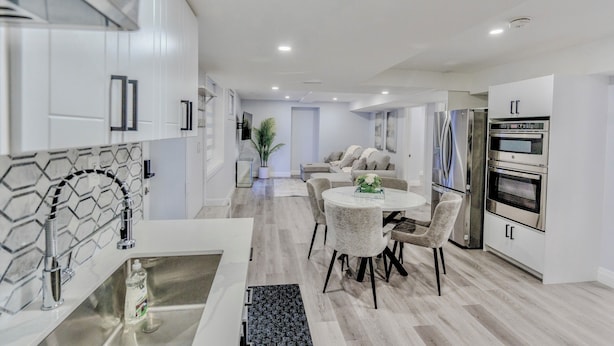 A modern kitchen with white cabinetry, a stainless steel sink, and a dining area with a round table and chairs. - Luxurious Unit in Hyde Park (London)
