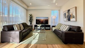 A modern living room with two leather sofas, a glass coffee table, a flat-screen TV, a potted plant, and a painting on the wall. - Aalto Retreat 3: Chic & Modern, Close 2 Everything (Rosebud)