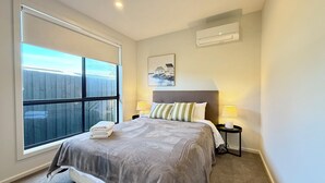 A bedroom with a large window, a bed with a grey blanket, two bedside lamps, and a wall-mounted air conditioner. - Aalto Retreat 3: Chic & Modern, Close 2 Everything (Rosebud)