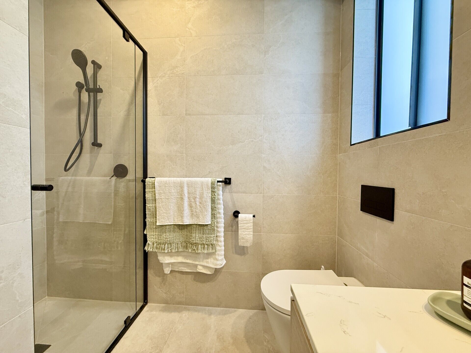 A modern bathroom with a glass-enclosed shower, a toilet, and a sink with a marble countertop.