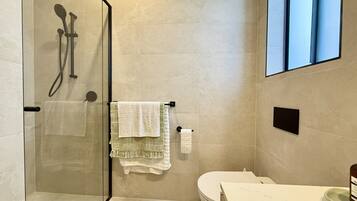 A modern bathroom with a glass-enclosed shower, a toilet, and a sink with a marble countertop.