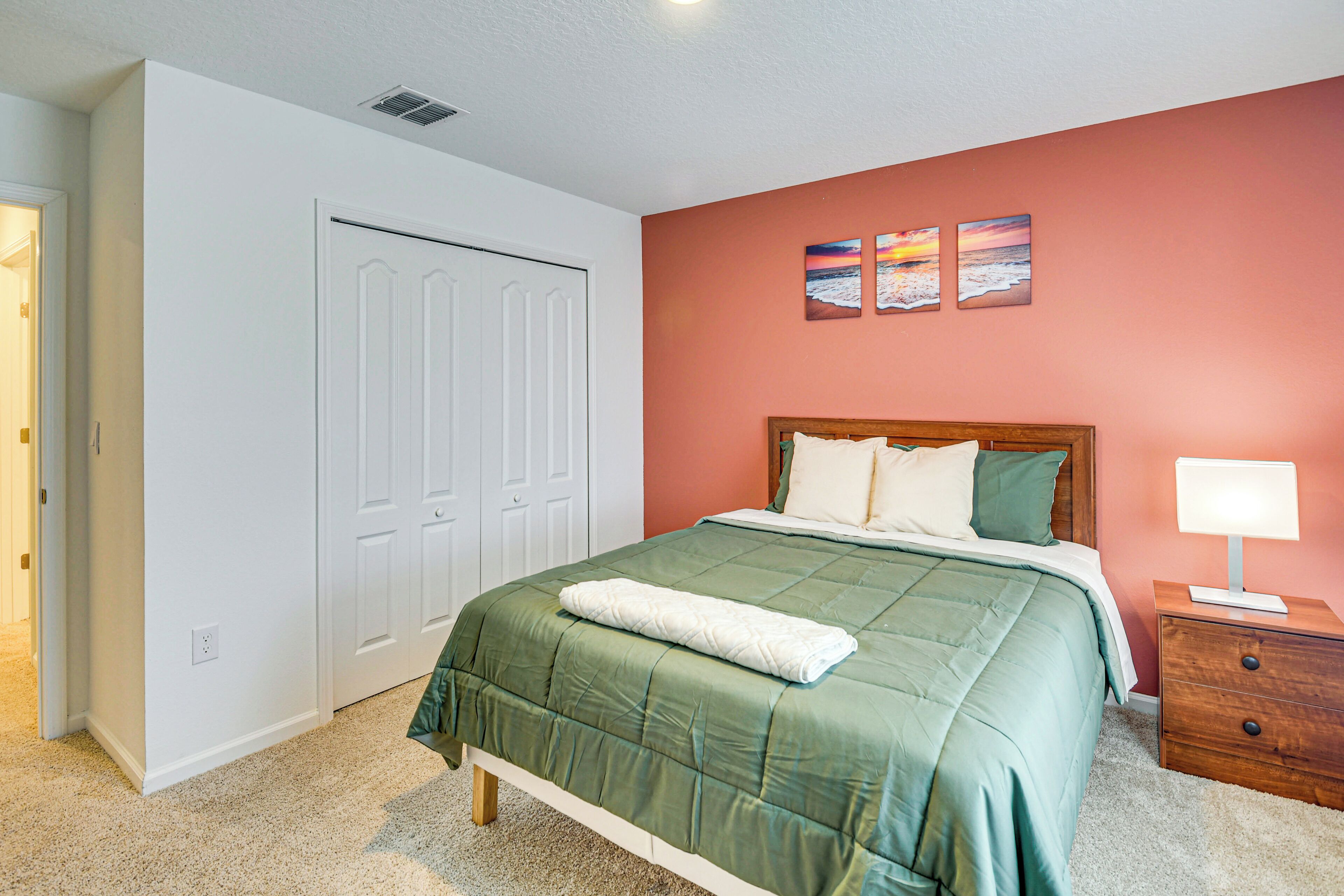 Une chambre avec une couvre-lit verte, des murs blancs, une tête de lit en bois, une table de chevet avec une lampe et une armoire aux portes blanches.