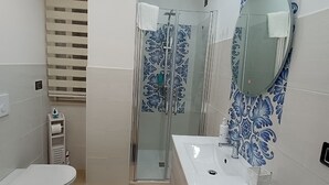 A modern bathroom with a glass-enclosed shower, a white sink, and a blue bath mat. - Triple room Tropea center (Tropea)