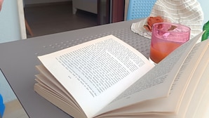A table with an open book, a glass of drink, and a plate with a flower. - Triple room Tropea center (Tropea)
