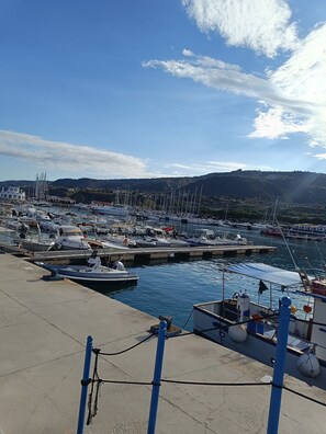 Ein Yachthafen mit vertäuten Booten, einer Betonmole und einer bergigen Landschaft im Hintergrund.