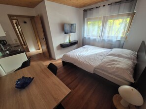 A hotel room with a bed, a desk, a chair, a TV, and a window with curtains. - Accommodation for nature lovers (Grömbach)