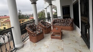Een overdekt balkon met rieten meubilair, een betegelde vloer en een uitzicht op de skyline.