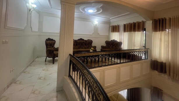 Een statige kamer met een marmeren vloer, een trap met een zwarte balustrade en een kroonluchter.