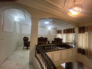 Una sala amplia con piso de mármol, una escalera con balaustrada negra y un candelabro.