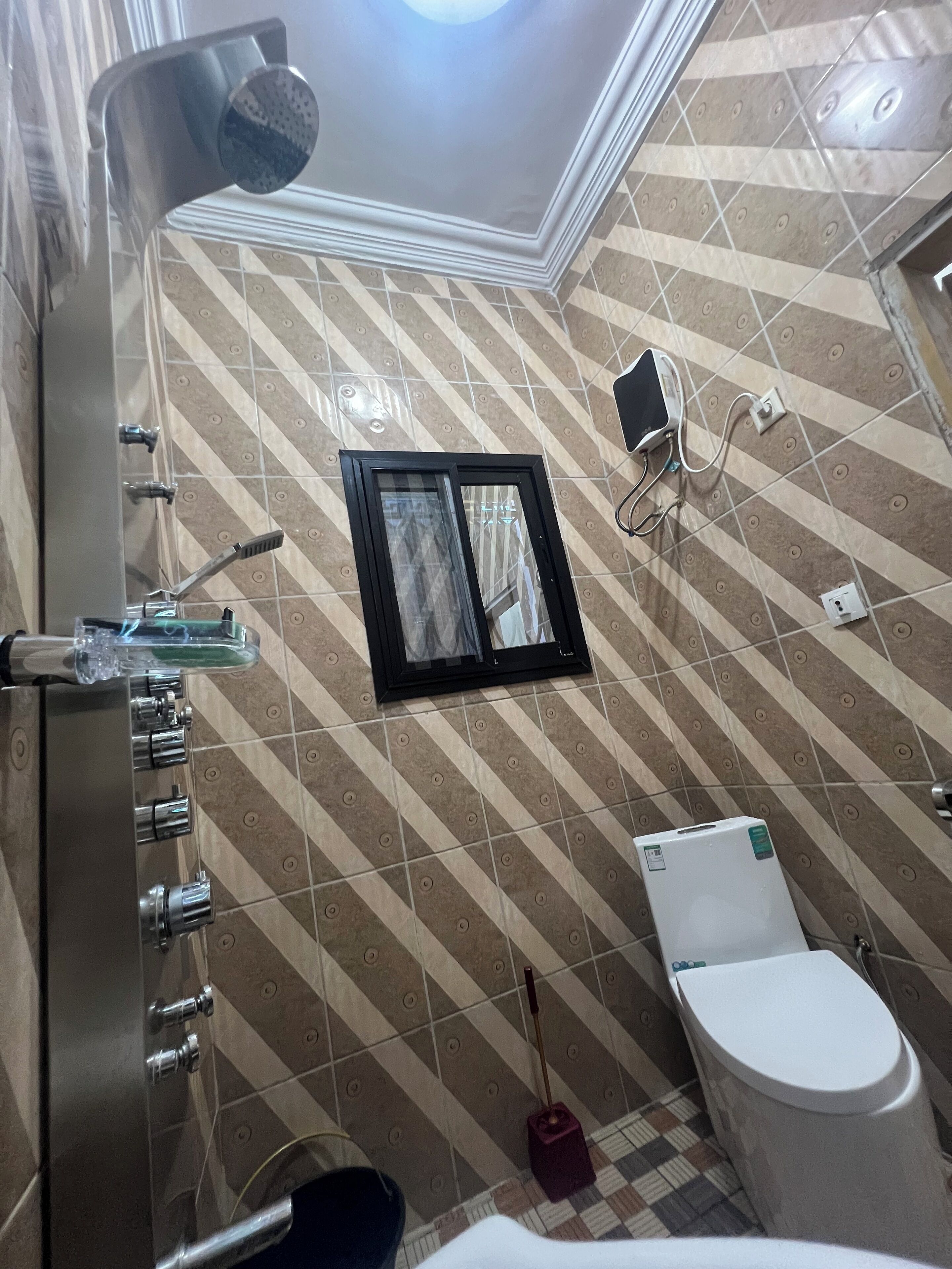 Un baño con ducha, inodoro, ventana y teléfono instalado en la pared.