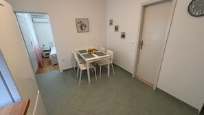 A small dining area with a table and chairs, a clock on the wall, and a door leading to another room. - Apartmani Vela Makarska (Makarska)