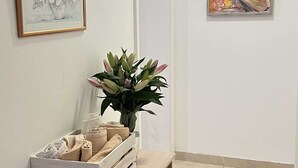 Un pasillo con un banco de madera, un jarrón de flores y dos cuadros en las paredes.