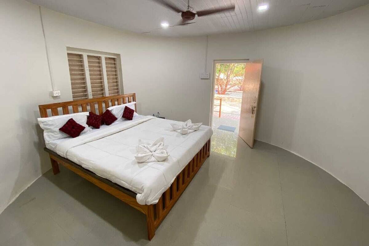 A clean, well-lit bedroom with a wooden bed, white linens, and a ceiling fan.