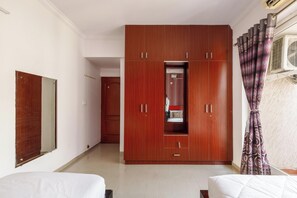 A bedroom with a wooden wardrobe, a bed, and a window with curtains. - The Crimson Cove (Bengaluru)