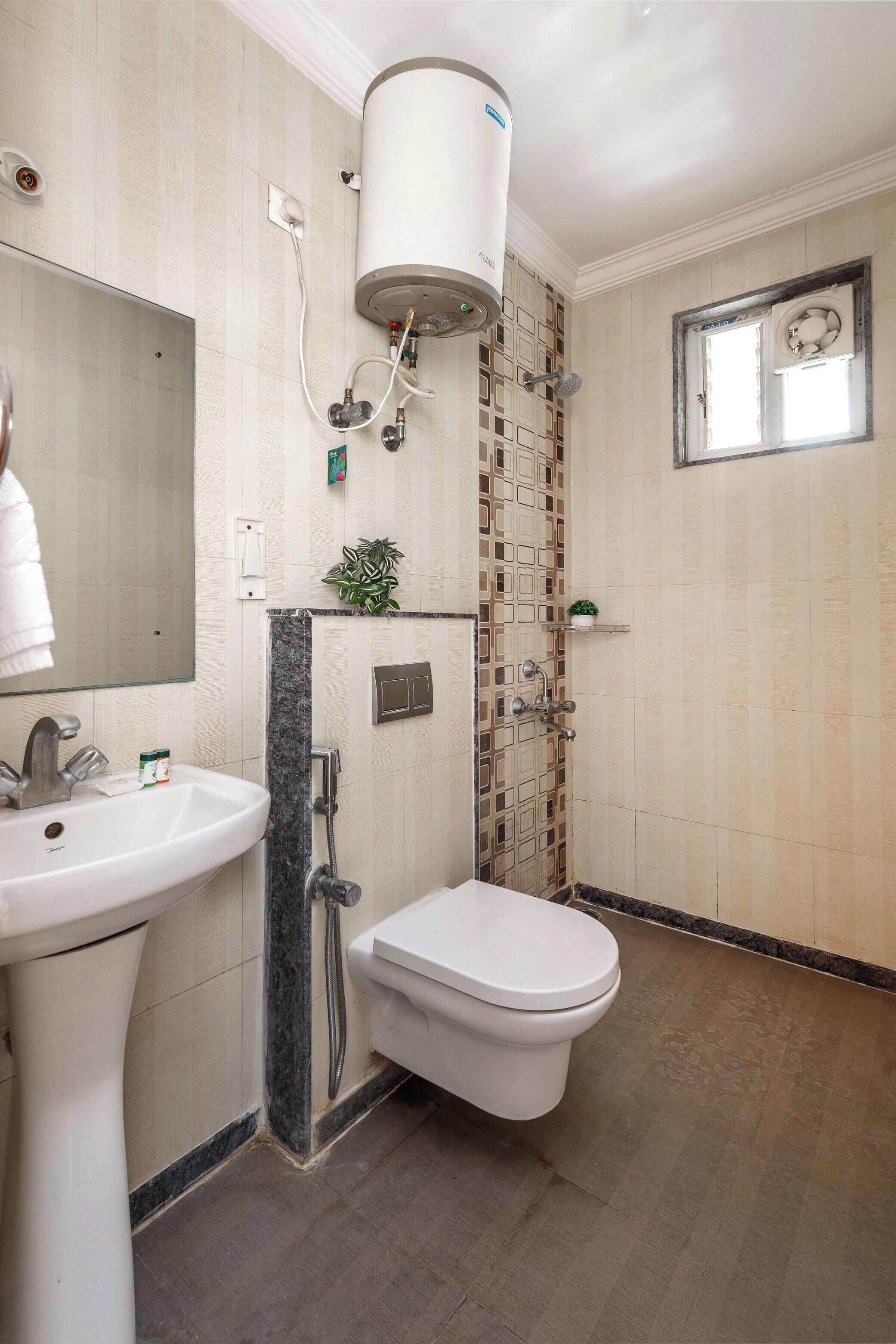 Une salle de bain avec un lavabo, des toilettes et une douche, le tout de couleur blanche. Un miroir se trouve au-dessus du lavabo et une fenêtre au-dessus de la douche.