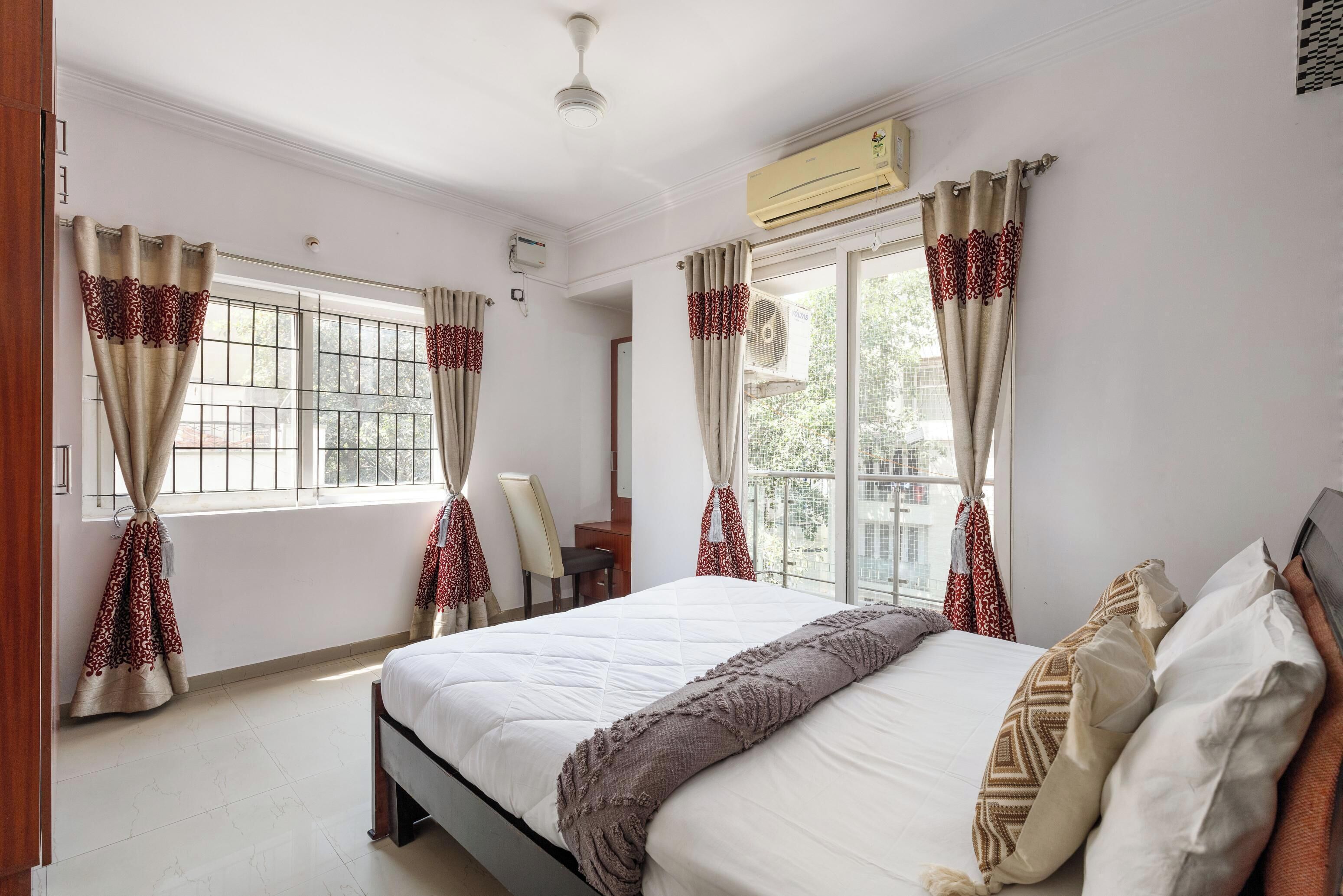 A hotel room with a bed, curtains, an air conditioning unit, and a window with a view.