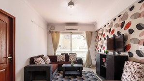 Un salon avec un canapé, une table basse, un téléviseur posé sur un meuble et un mur décoré d’un motif.