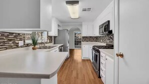A modern kitchen with white cabinetry, a central island, a stainless steel refrigerator, and a microwave. - Cozy 3BDR/2BATH in N Phoenix. 8mi from Mayo Clinic (Phoenix)