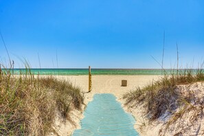 Un sentier qui longe la plage et mène à l’océan, avec des dunes de sable et un poteau en bois.