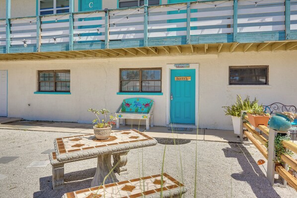 Un bâtiment avec une porte bleue portant l’inscription « BETTYS », un petit espace extérieur aménagé avec une table et des chaises, et des plantes en pot.