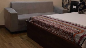 A room with a bed, a sofa, a patterned wall, and a wooden floor. - Satyam Dham (Vrindavan)