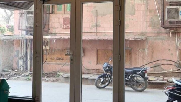 A hotel entrance with a glass door, a green mat, and a street view outside. - Satyam Dham (Vrindavan)