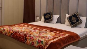 A hotel room with a bed, a wooden headboard, and a door. - Satyam Dham (Vrindavan)