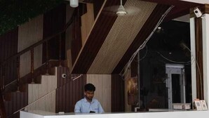 A reception desk with a wooden finish, a white counter, and a large window. - Satyam Dham (Vrindavan)