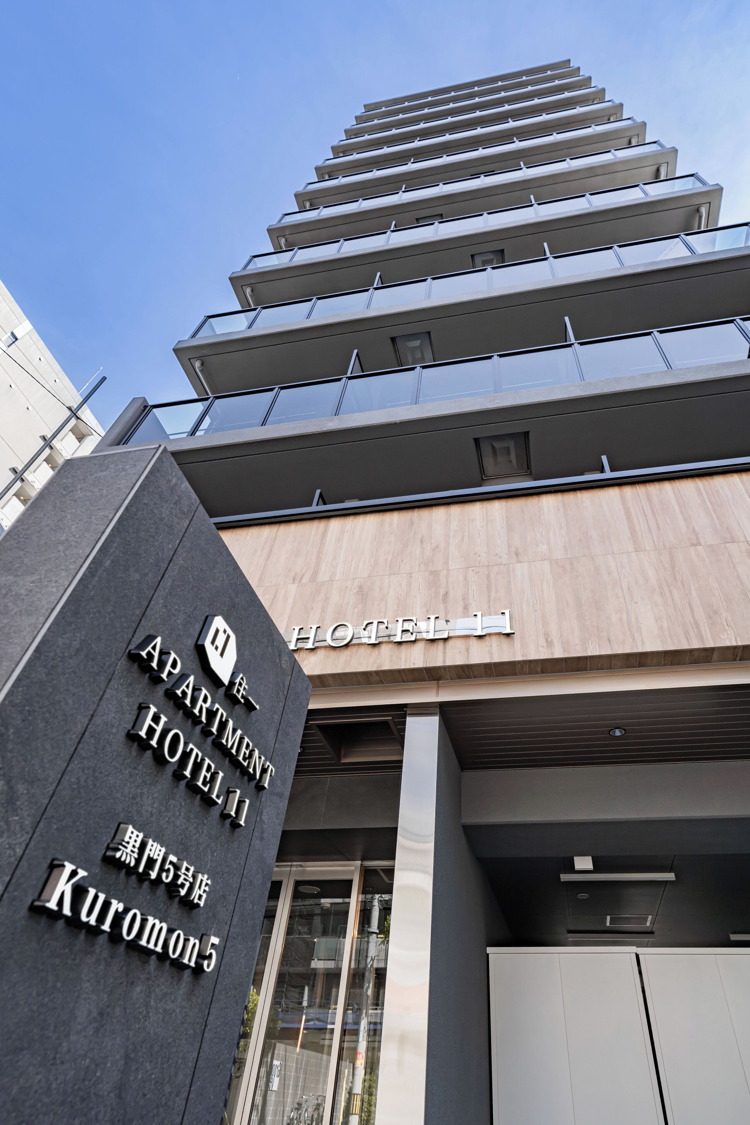 A hotel entrance with a modern design, featuring a prominent sign for the 'APARTMENT HOTEL' and a visible address 'Kuromon 5-5'.