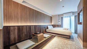 A modern hotel room with a large bed, a bedside table, a small stool, and a large window with curtains.