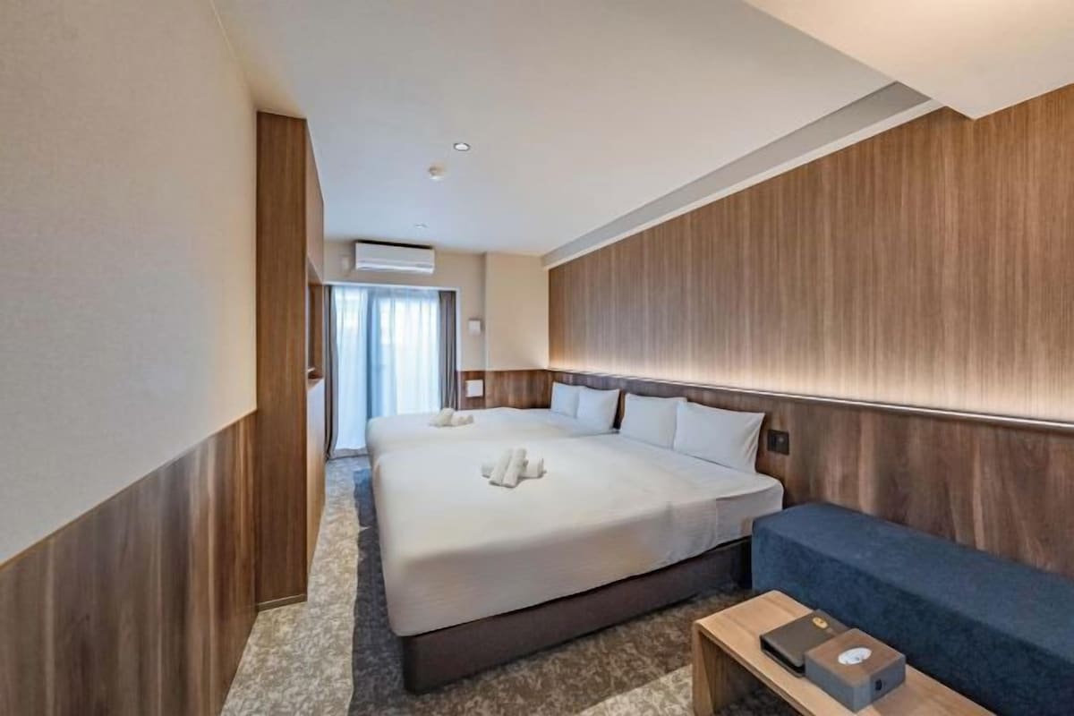 A hotel room with a large bed, a sofa, a small table, and a window with curtains.