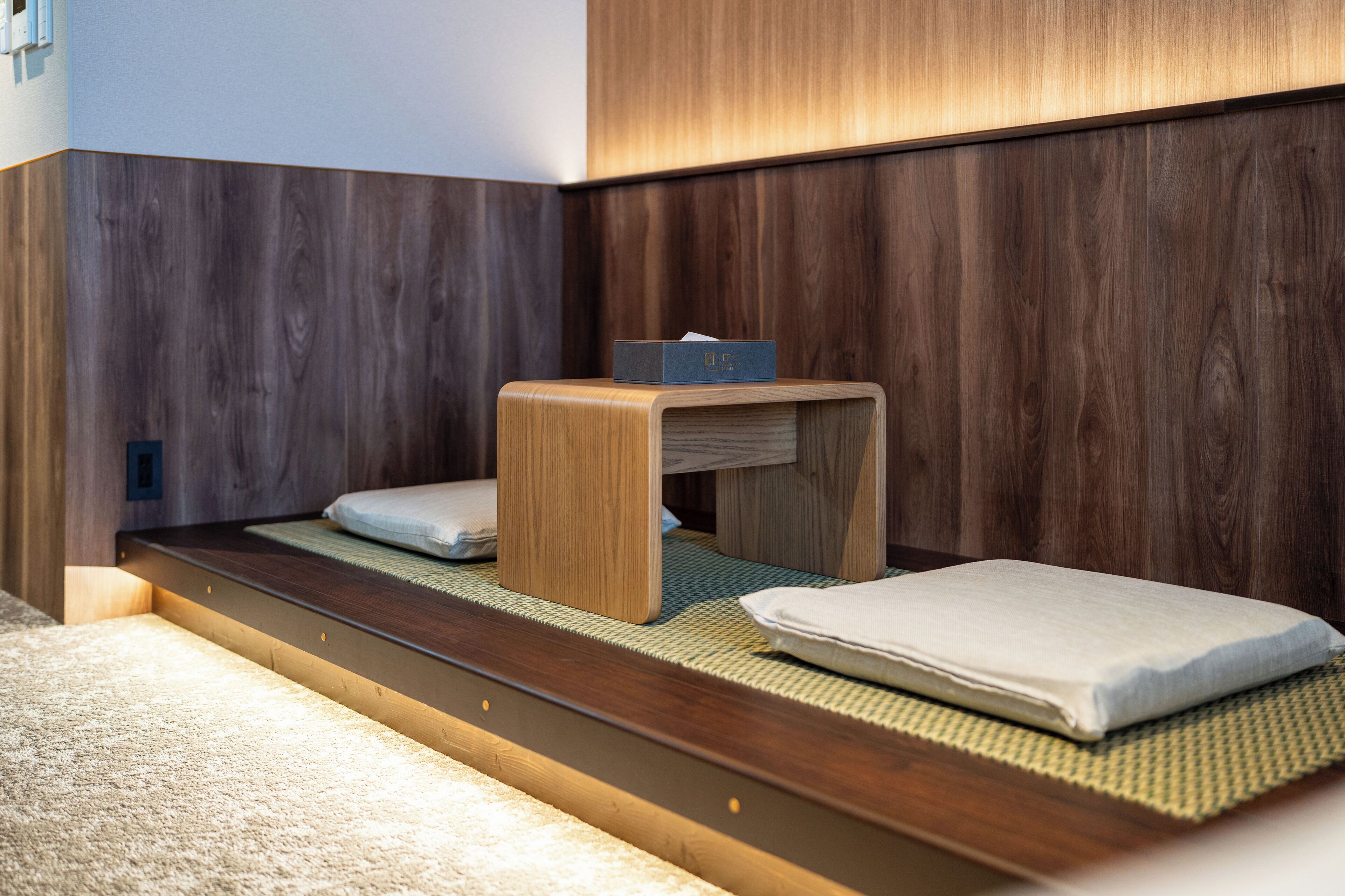 A compact, modern room with a low platform bed, a small wooden table, and a wall-mounted shelf.