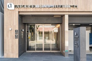 L’entrée d’un hôtel-résidence à l’architecture moderne, caractérisée par une porte d’entrée en verre offrant une vue dégagée sur l’intérieur.