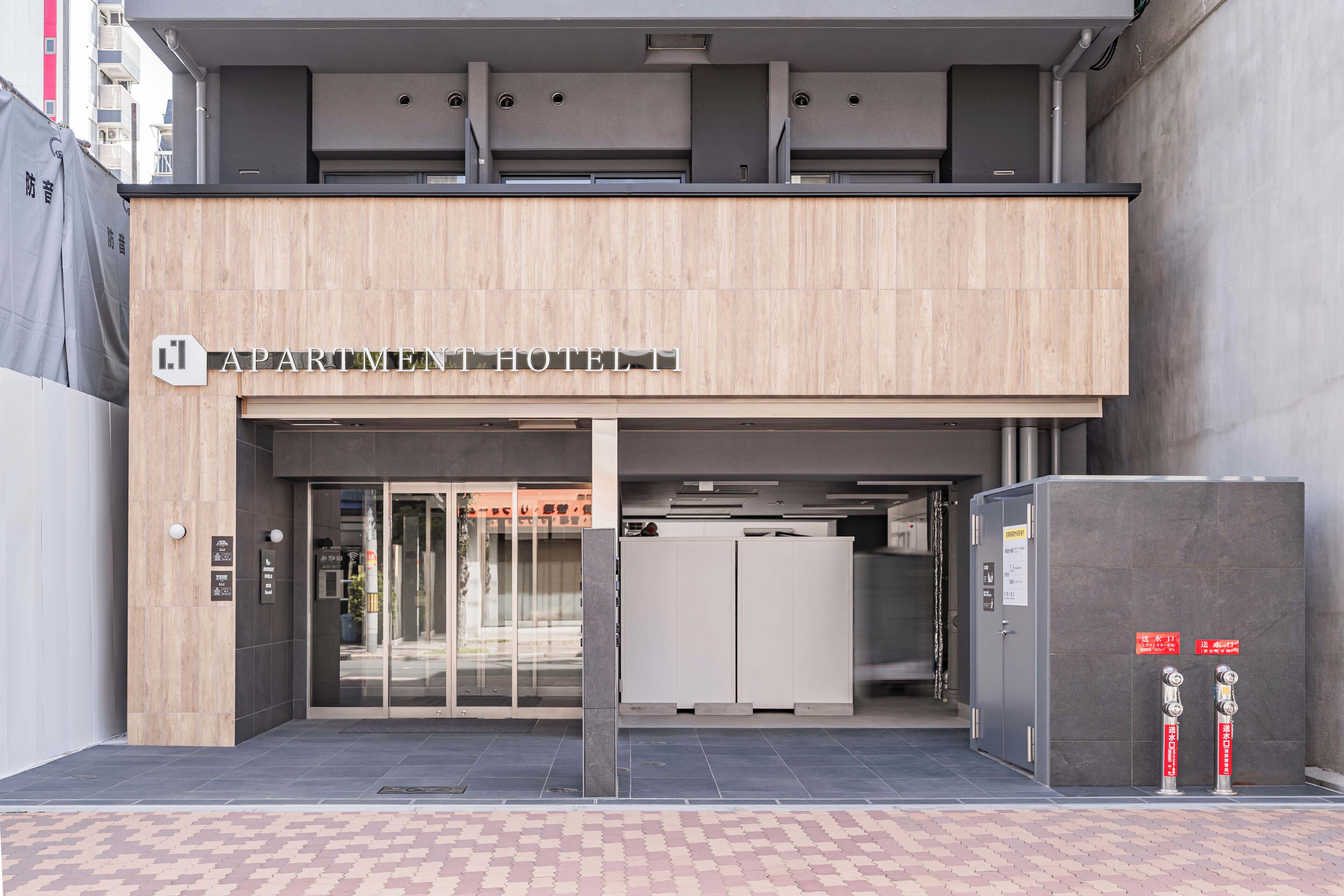 A modern hotel entrance with a sign, glass doors, and a fire safety cabinet.