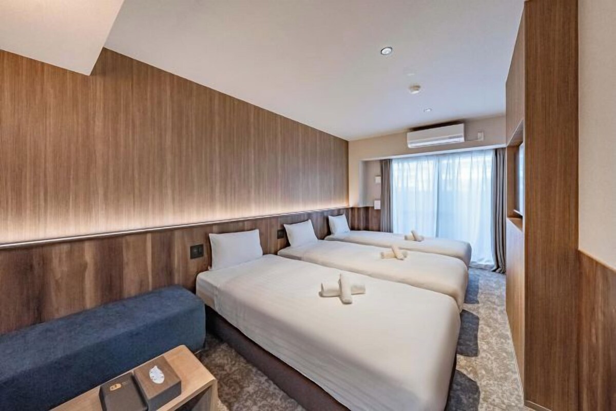 A hotel room with three beds, a seating area, and a wooden panel wall.