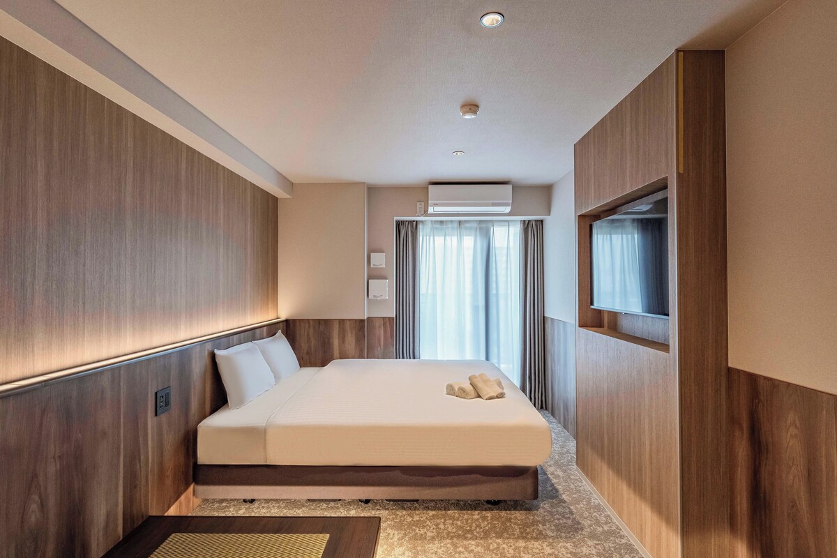 A modern hotel room with a large bed, wooden paneling, a flat-screen TV, and an air conditioning unit.