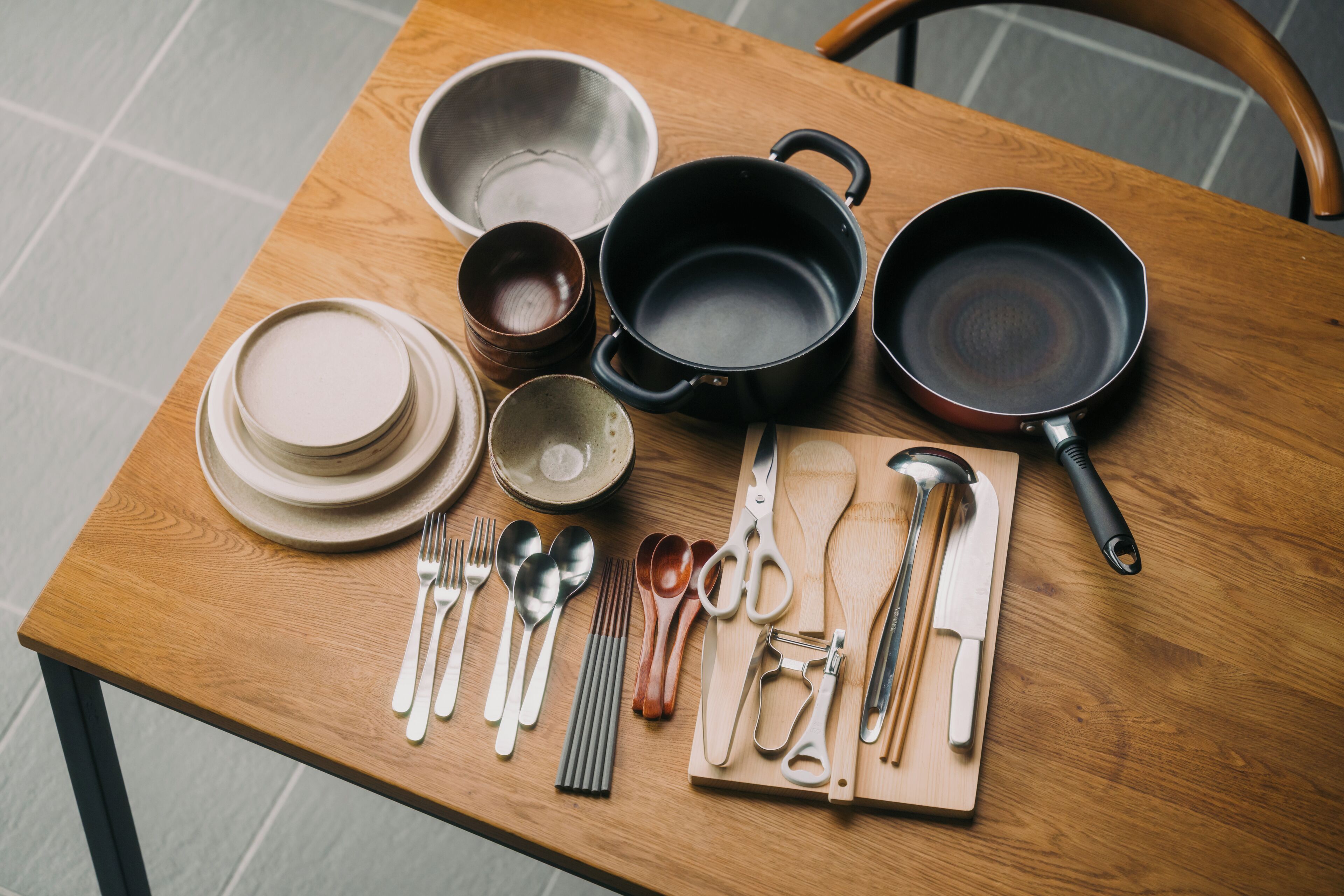 A wooden table with various kitchen utensils and cookware.