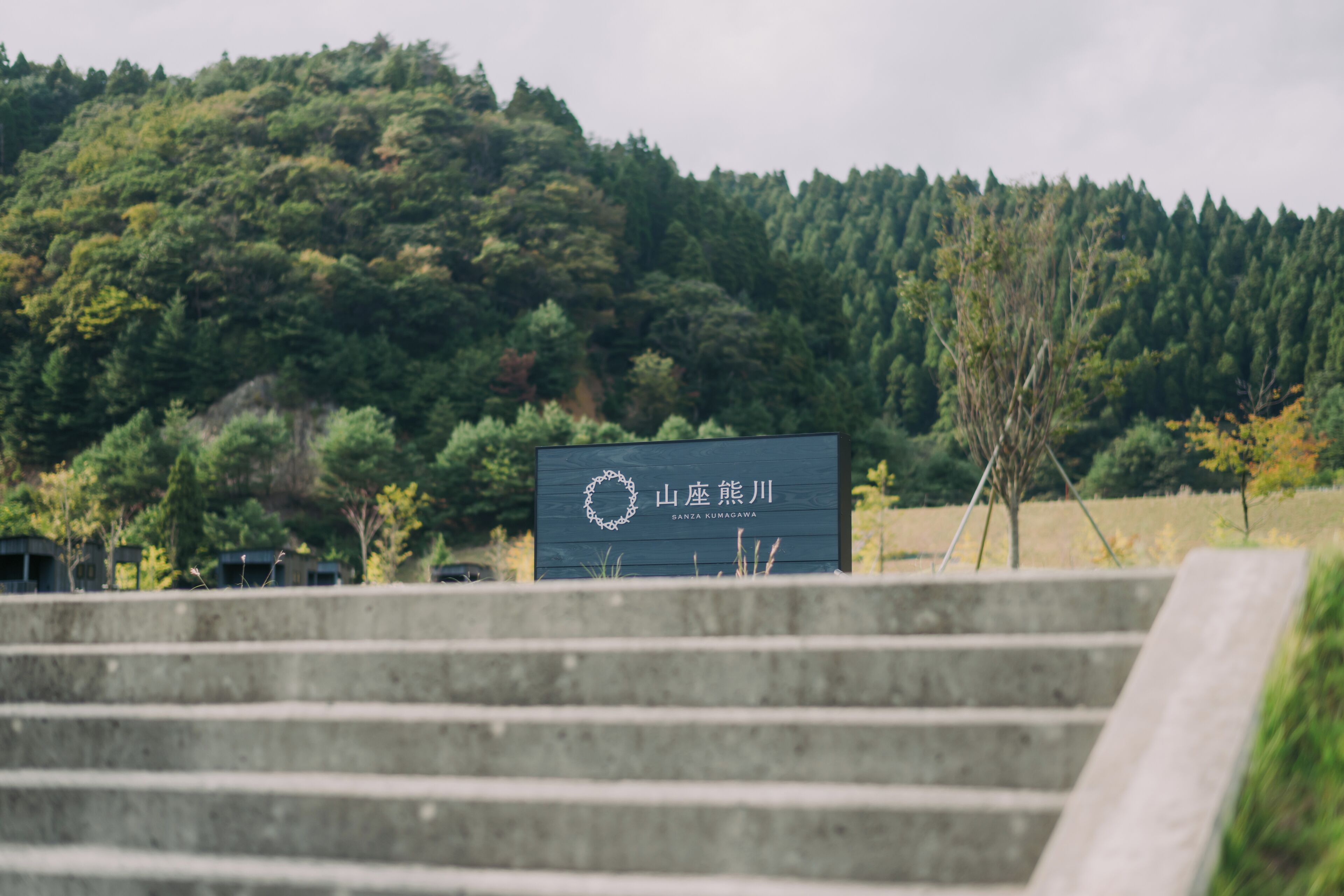 A sign with Japanese characters on a concrete structure, surrounded by a forested hillside.