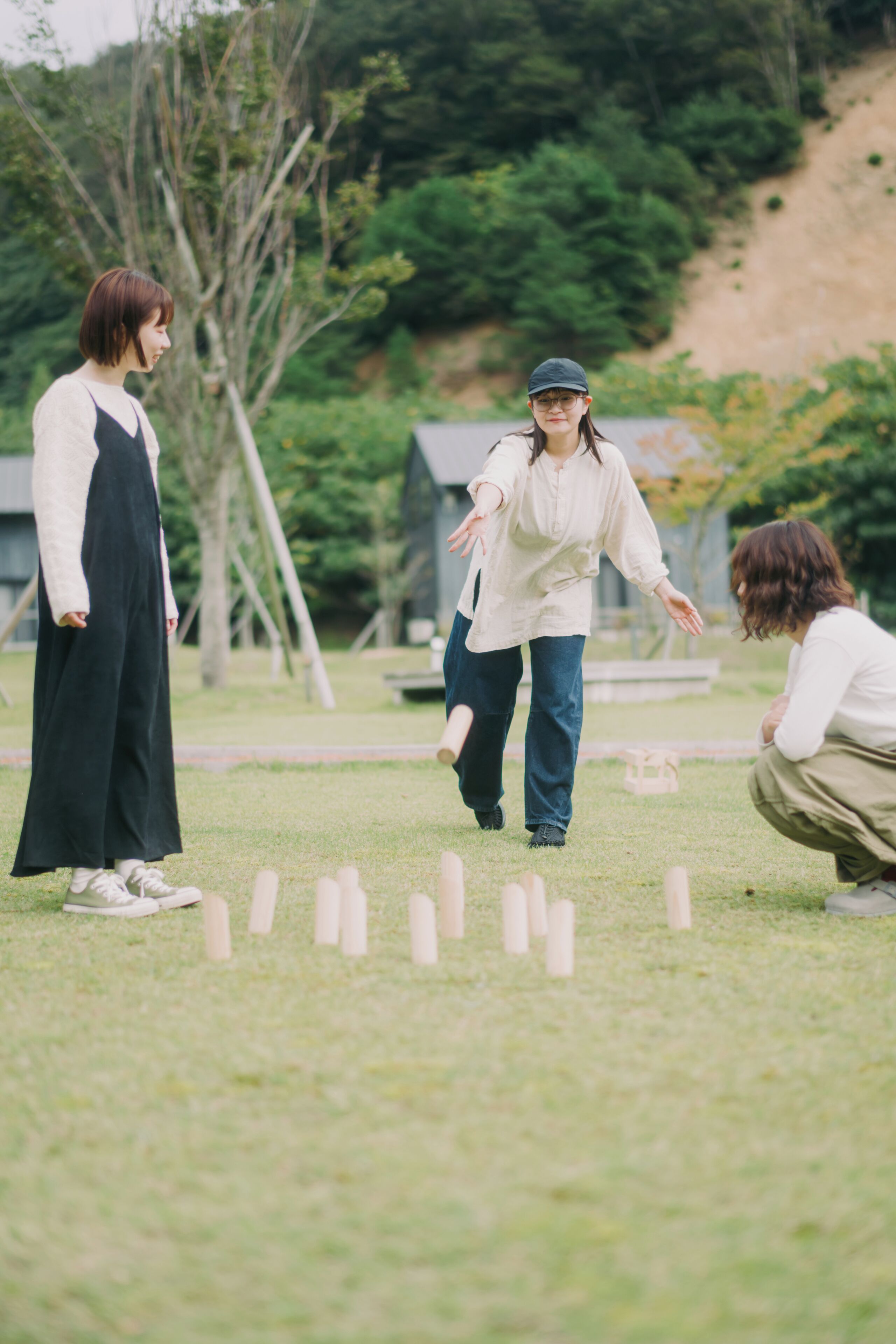 Three people playing a game with wooden sticks on a grassy field.